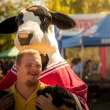 Chłopak z trisomią przytulany od tyłu przez dużą maskotkę krowę.