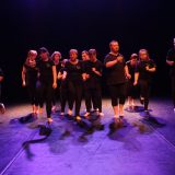 Grupa na scenie w ruchu tanecznym.