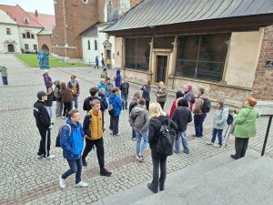 Grupa ludzi na kamiennym dziedzińcu przed dużą budowlą.