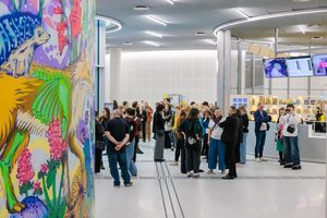 Dużo ludzi w nowoczesnym, jasnym wnętrzu. Widać fragment ściany pomalowanej jaskrawo w motywy zwierząt i roślin, w głębi lada, ekrany i przedmioty wyeksponowane na półkach.
