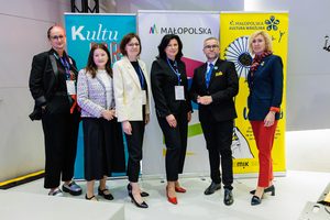 6 osób pozuje na tle banerów Województwa Małopolskiego, Małopolskiego Instytutu Kultury i Festiwalu Kultury Wrażliwej. Są elegancko ubrane i mają identyfikatory na niebieskich smyczach.