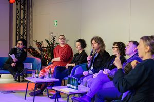 Kilka osób siedzi na kanapach na scenie. Dwie z nich mówią do mikrofonów, z brzegu siedzi tłumaczka na język migowy. Z przodu na stolikach stoi woda w butelkach dla rozmówców.