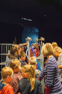 Grupa dzieci we wnętrzu. Tłoczą się wokół wysokich metalowych klatek z przyczepionymi gumowymi rurkami. Każde chce dotknąć konstrukcji, zobaczyć z bliska. Pomagają im osoby dorosłe.